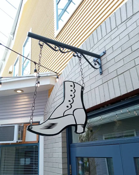Wood top button boot cutout sign hanging outside of the building