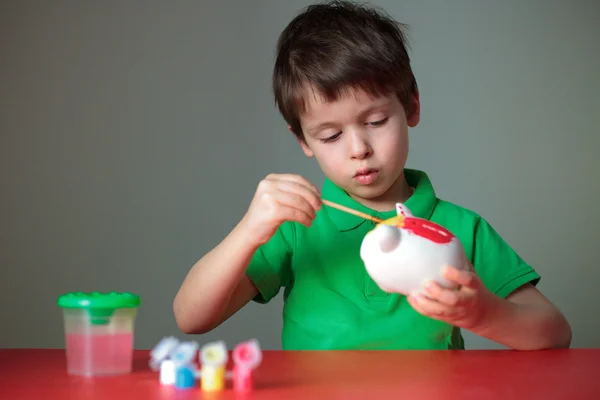 Bonito menino pintando seu brinquedo porquinho — Fotografia de Stock