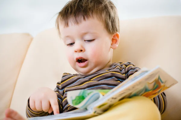 Netter kleiner Junge liest Buch auf dem Sofa — Stockfoto