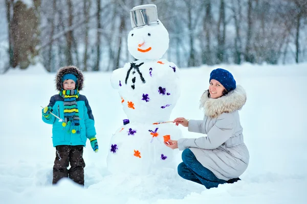 Mamma och hennes lilla son målning en snögubbe — Stockfoto