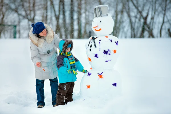 Kleine jongen met zijn moeder schilderen een sneeuwpop — Stockfoto