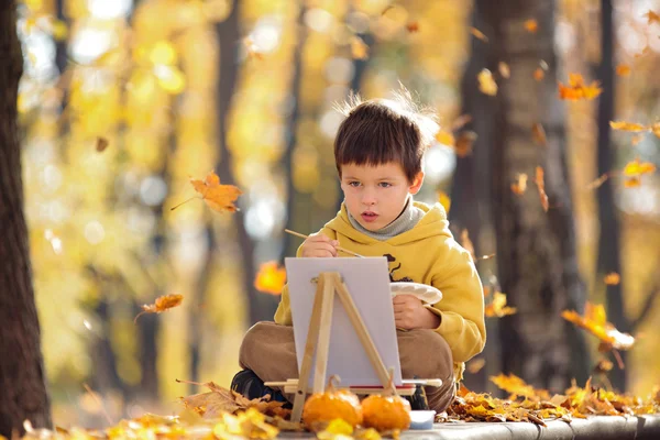 Cute little boy painting in golden autumn park — Stock Photo, Image