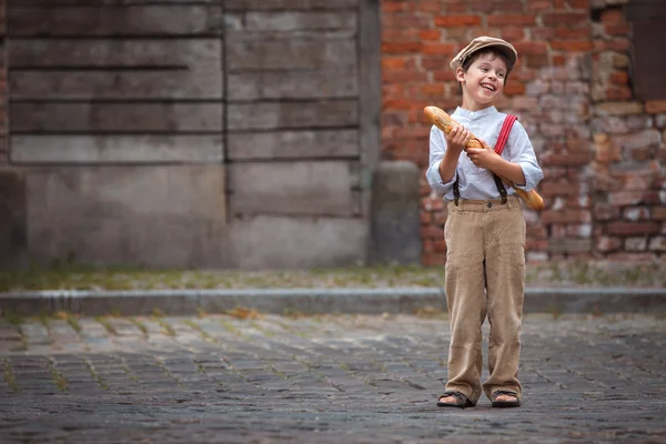 Веселый улыбающийся мальчик с багетом на открытом воздухе — стоковое фото