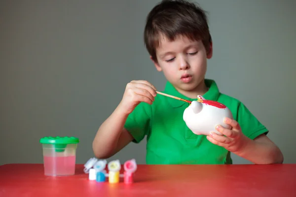 Bonito menino pintando seu brinquedo porquinho — Fotografia de Stock