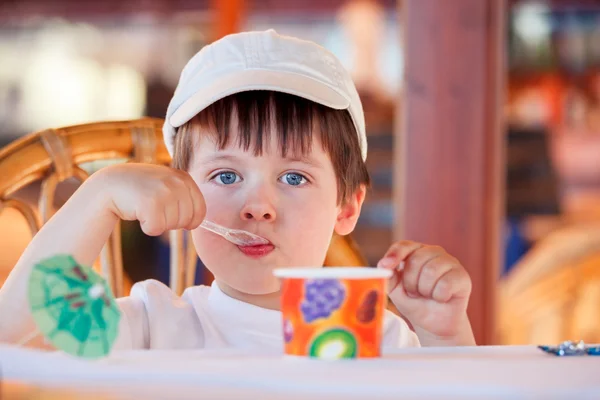 Aranyos kisfiú eszik fagylaltot, beltéri kávézóban — Stock Fotó