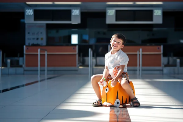 Netter kleiner Junge mit orangefarbenem Koffer am Flughafen — Stockfoto