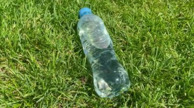 Açık havada, parlak güneş ışığında yeşil çimlerin üzerinde duran bir şişe temiz su. Açık hava sporu yapıyorum. Sıcak hava konseptinde susuzluk ve su dengesi. Bir şişe şeffaf plastik su..