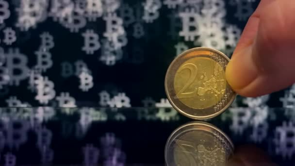 ビットコインのシンボルを持つ暗い背景に手に2ユーロコイン コインが落ちてる 暗号通貨交換レート — ストック動画