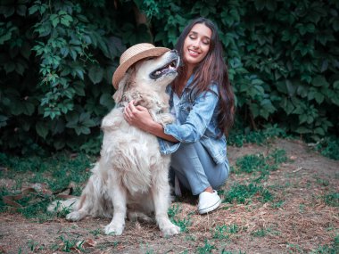 Golden Retriever labrador köpeği ve hasır şapkayla oynayan genç mutlu kadının portresi.