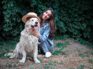 Golden Retriever labrador köpeği ve hasır şapkayla oynayan genç mutlu kadının portresi.