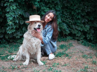 Golden Retriever labrador köpeği ve hasır şapkayla oynayan genç mutlu kadının portresi.