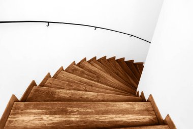 Özel bir evdeki ahşap bir sarmal merdivenin en üst görüntüsü. Beyaz duvarlar