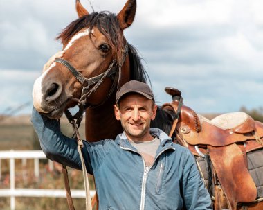 Tahta çitlerin yanında kahverengi atı olan bir binicinin portresi. İnsan ve hayvan dostluğu.