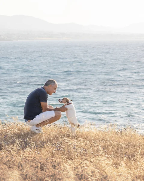 Elderly 60-years old man sitting with his dog near the sea.