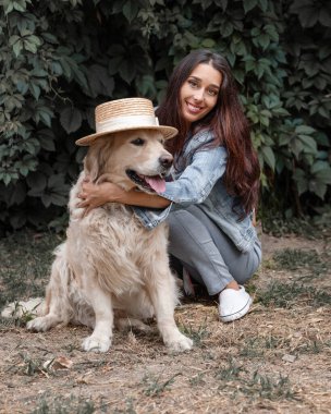 25-30 yaşlarında gülümseyen genç bir kadının yakın plan portresi yaz parkında sevimli köpeği Golden Retriever Labrador 'u kucaklıyor.