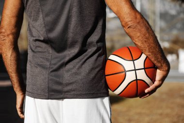 Close-up basketball ball in right hand of adult man standing backwards outdoor.
