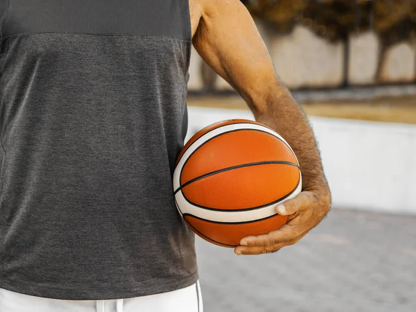 Close-up basketball ball in left hand of adult man outdoor.
