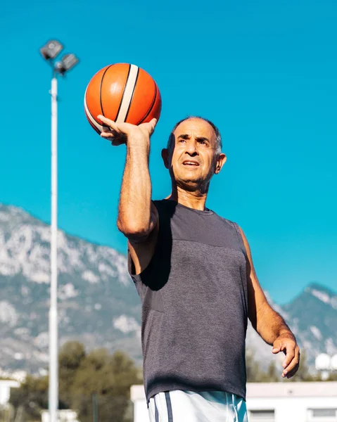 Half-length portrait of 60-years old basketball player in good shape ready to shoot a sport ball into hoop outdoor