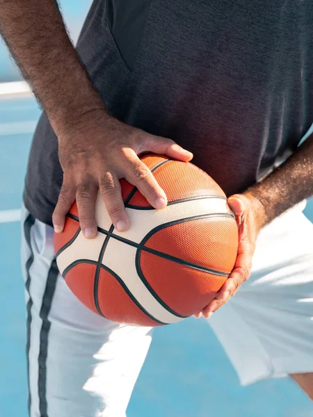 Closeup image of hands of adult basketball player holding a orange sport ball at waist level ready to pass it.