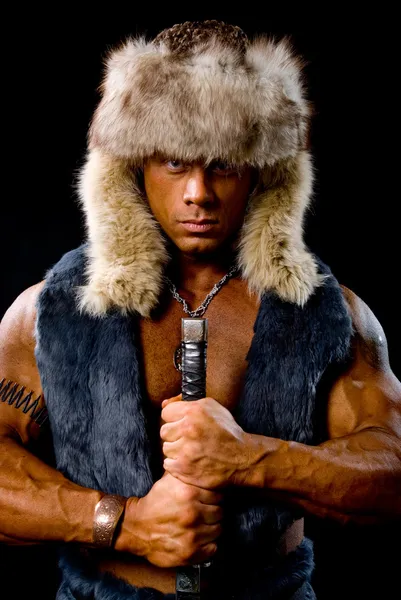 Muscular man warrior with a sword in a fur hat — Stock Photo, Image