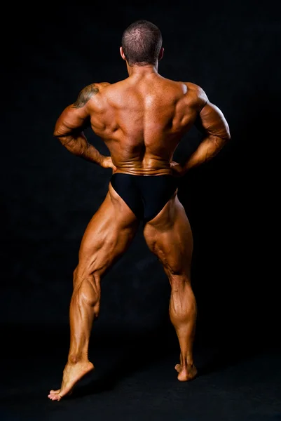 皮肤晒得黝黑的健美运动员显示的武器和背部的肌肉 — 图库照片