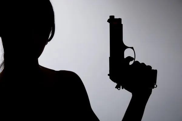 Silhouette d'une femme avec un pistolet sur un fond gris — Photo