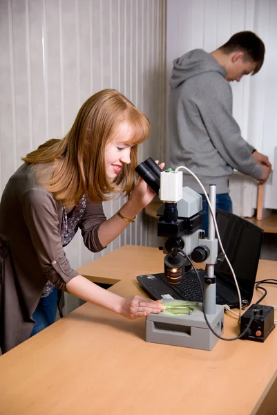 Junge Frau blickt durch Mikroskoplinse — Stockfoto