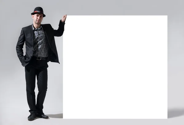 A man in a hat stands next to a blank billboard — Stock Photo, Image