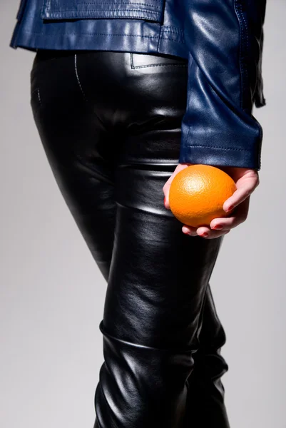Το κορίτσι στο μαύρο δερμάτινο παντελόνι με ένα πορτοκάλι στο χέρι του — Φωτογραφία Αρχείου