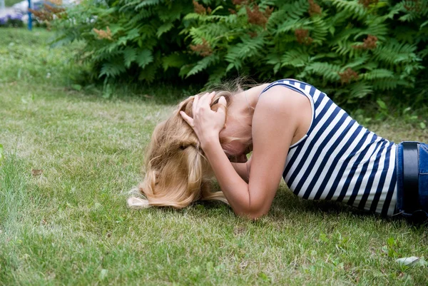 Dziewczyna leżąc na trawie i chwycił się rękami za głowę. — Zdjęcie stockowe
