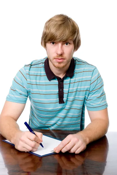 Młody człowiek siedzi przy biurku z piórem w ręku. — Zdjęcie stockowe