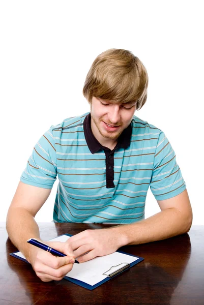 Wesoły młody mężczyzna siedzący przy biurku z piórem w ręku. — Zdjęcie stockowe