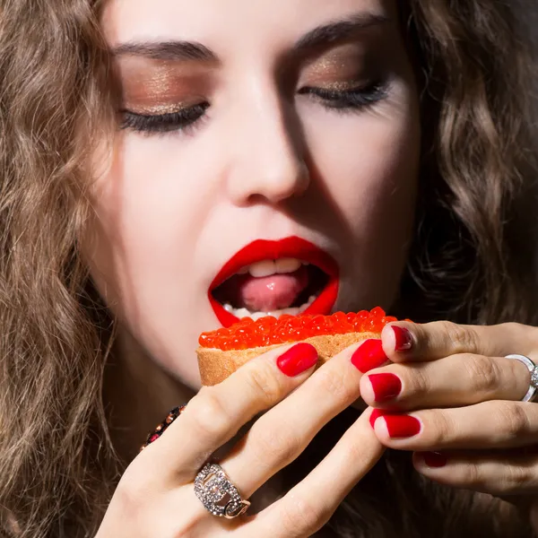 Mooi meisje eet een sandwich met rode kaviaar. — Stockfoto