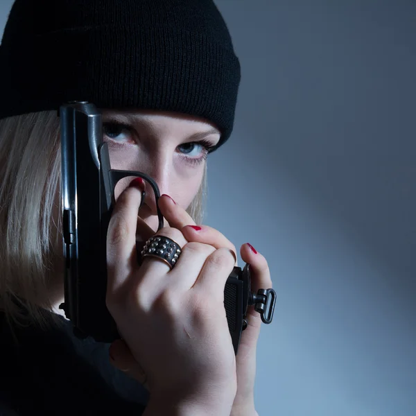 Jeune fille dans une casquette sombre avec un pistolet à la main. avec bras — Photo