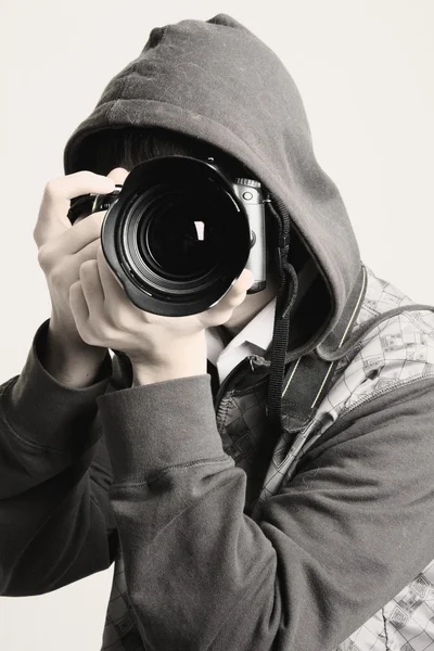 A young man in a hood using a professional camera — Stock Photo, Image