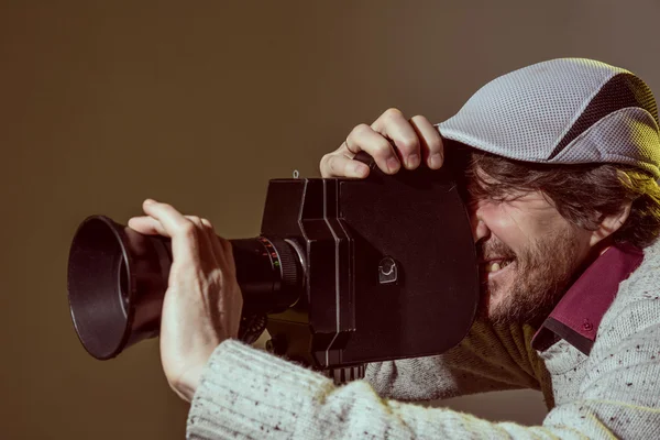 En man klädd i en mössa med en gammal filmkamera — Stockfoto