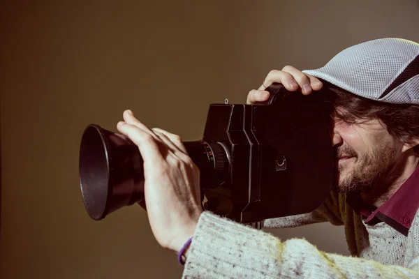 A man wearing a cap with an old movie camera. — Stock Photo, Image
