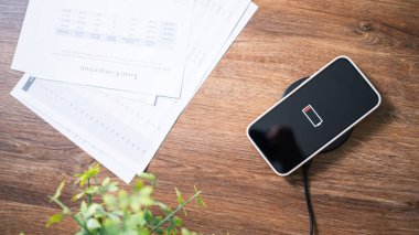 Masada kablosuz şarj cihazıyla cep telefonu bataryası şarj ediliyor. Akıllı telefon şarj cihazına yükleniyor. Kablosuz şarj cihazının yanındaki cep telefonu Modern yaşam tarzı teknolojisi 