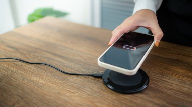 Masada kablosuz şarj cihazıyla cep telefonu bataryası şarj ediliyor. Akıllı telefon şarj cihazına yükleniyor. Kablosuz şarj cihazının yanındaki cep telefonu Modern yaşam tarzı teknolojisi 