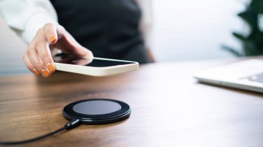 Masada kablosuz şarj cihazıyla cep telefonu bataryası şarj ediliyor. Akıllı telefon şarj cihazına yükleniyor. Kablosuz şarj cihazının yanındaki cep telefonu Modern yaşam tarzı teknolojisi 
