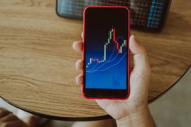 Yatırımcı telefonu elinde tutuyor ve borsa forksu veya kriptografi için uygun olan şamdan grafiklerine bakıyor. Finansal yatırım grafikleri, Mali Ekonomi eğilimleri, Borsa Konsepti