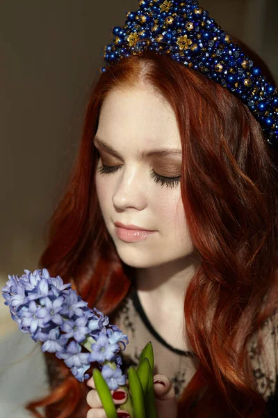 Una mujer pelirroja con los ojos cerrados. Sostiene una flor azul jacinto. En la cabeza de la diadema es azul. — Foto de Stock