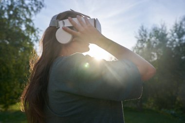 Elleriyle sanal gerçeklik gözlüğü takan kız yeşil ağaçların arka planında duruyor. Gelecek kavramı..