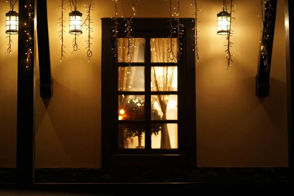 Уютный дом с гирляндами, окно со светом, фон для рождественского настроения — стоковое фото