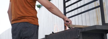 Bir adamın eli şöminenin üstünde kare barbekü ızgarası tutuyor. Barbeküye hazırlanma konsepti