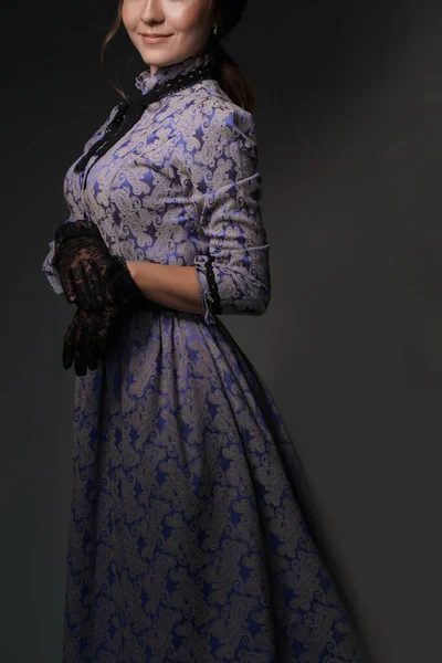 Une fille debout dans une robe bleue dans le style des années 1900, dans une robe rétro, un chapeau sur un fond gris. Mode historique du XIXe siècle — Photo