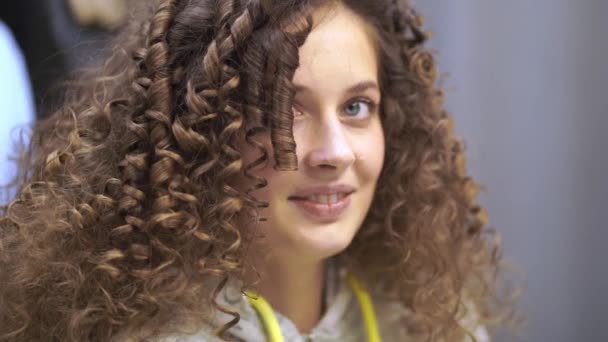 Close-up of a happy young woman with curly hair, she looks at the camera, smiles and blinks often — Stock Video