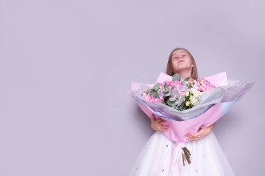 Beyaz elbiseli bir kız yan tarafta duruyor ve bir buket çiçek tutuyor, gözleri kapalı. Tatil kavramı