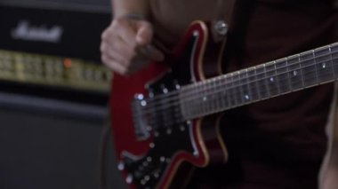 Elektronik gitar çalan bir adamın yakın çekimi var. Arka planda, bir ses yükseltici, bir ses sistemi. Ses konser ekipmanı.