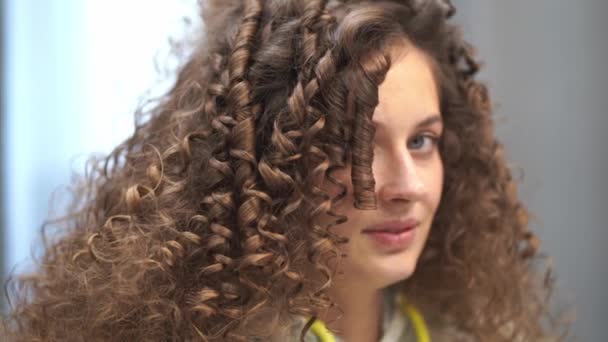 Detailní záběr mladé ženy s kudrnatými vlasy, která si češe vlasy, směje se do kamery a otáčí hlavou různými směry — Stock video